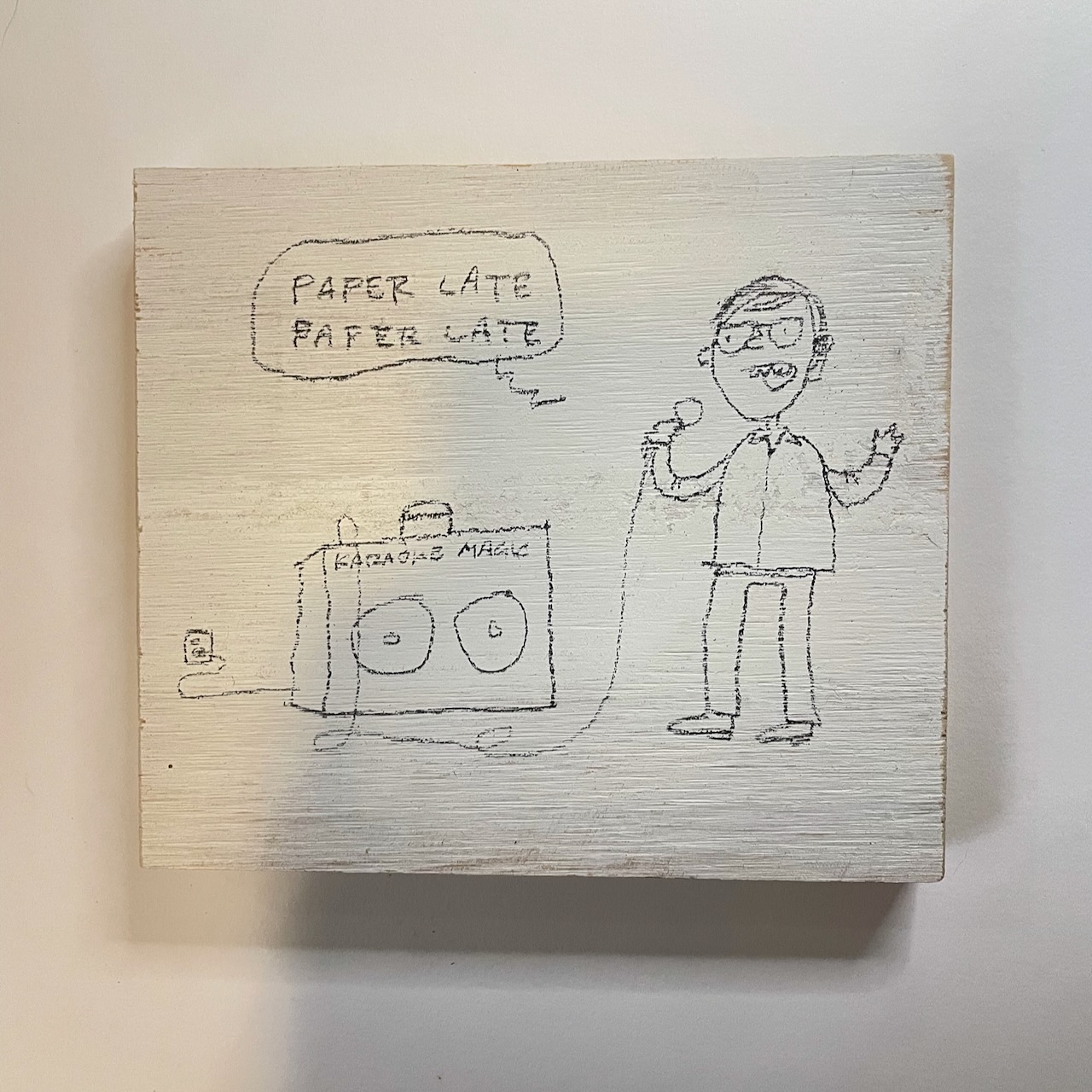 Cartoon by David Rhoden of man singing Genesis' "Paperlate" on an imaginary home karaoke machine. Cartoon is on a piece of painted plywood/